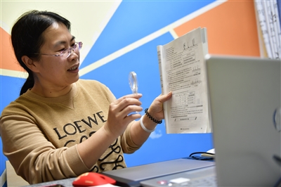 妻子王之玲拿著教材，在電腦前上初三物理課。